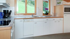 Una cocina moderna con armarios blancos, lavavajillas integrado, cafetera y ventana con vistas a un paisaje verde.