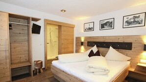 A wooden bed with white linens, a wooden wardrobe, a shower, and three framed pictures on the wall.