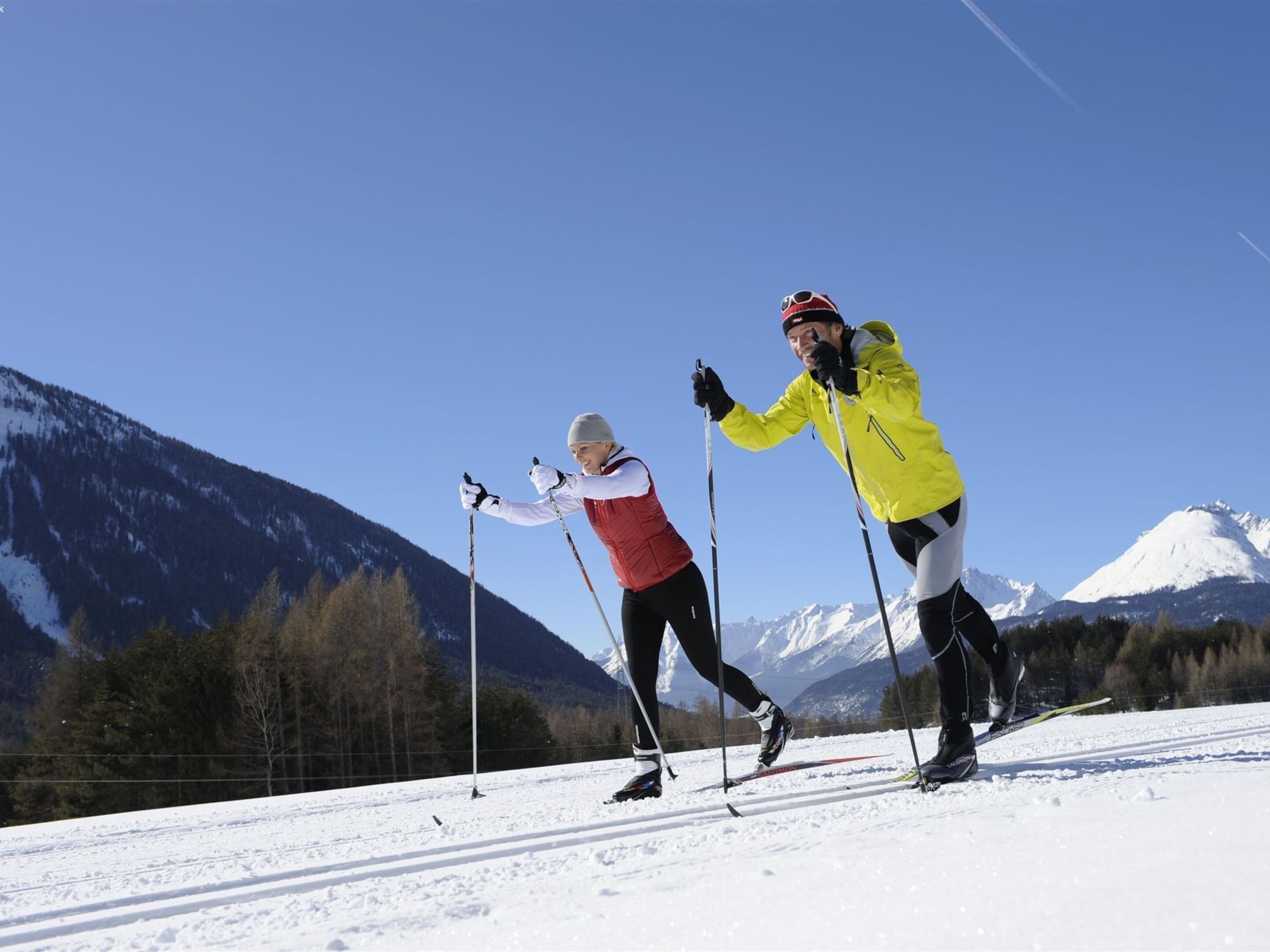 Two skiers on a snowy slope with mountains in the background.