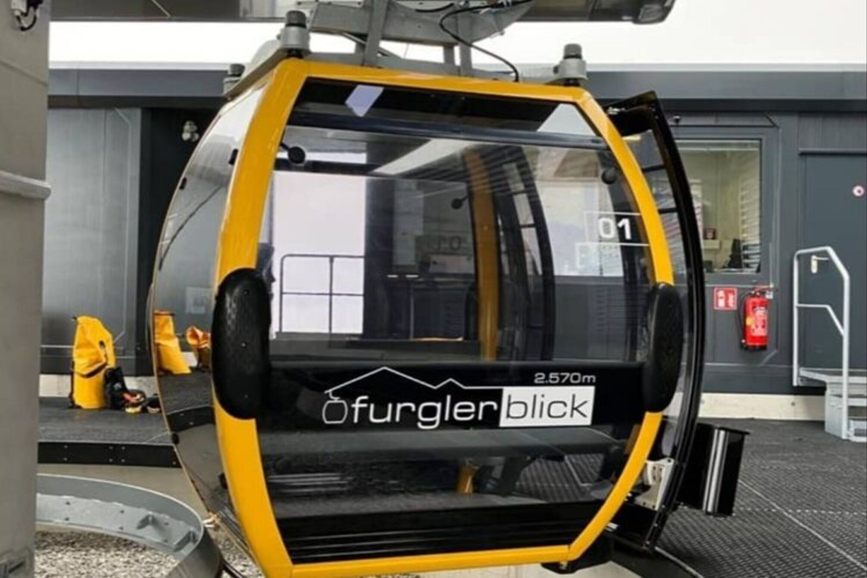 A yellow and black vehicle with "Ofurgerlblick" and "2.570m" text, parked outside a building with a fire extinguisher and a door marked "01".