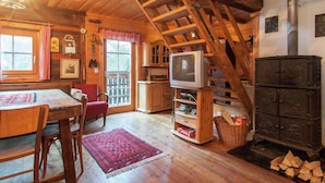A rustic cabin interior with a wooden staircase, a television, a fireplace, and a dining area with a red rug. - Chalet Near Lake Klopeiner With Sauna (Feistritz ob Bleiburg)