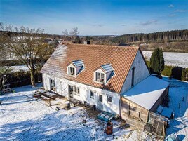 Una casa de dos pisos con techo inclinado, un pequeño garaje adosado y un patio cubierto de nieve.