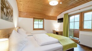A bedroom with two beds, wooden ceiling, a desk, a chair, and a window with curtains. - Spacious Chalet near Ski Area in Saalbach-Hinterglemm (Viehhofen)