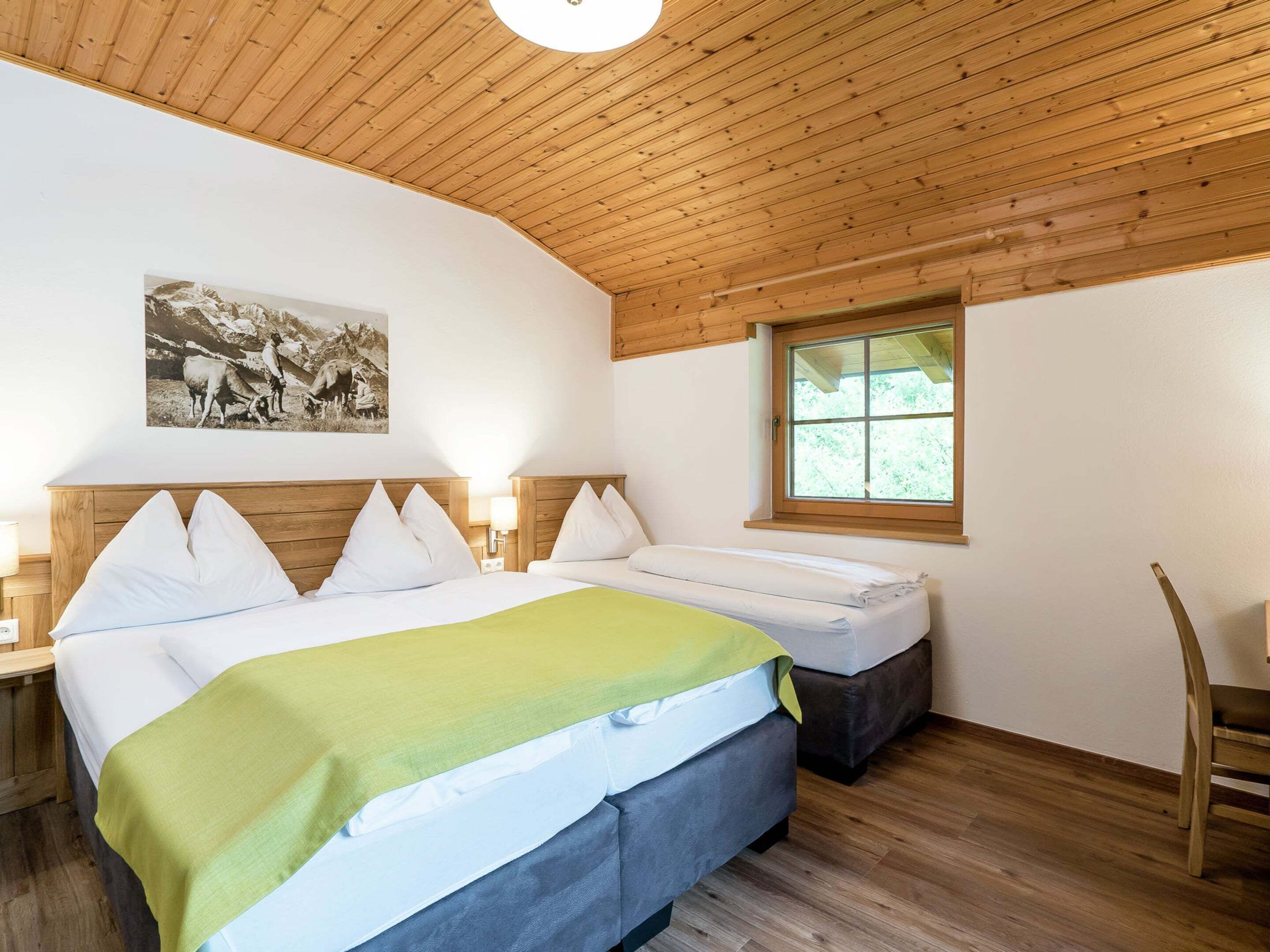 A room with a bed, a bedside table, a lamp, a window, and a picture on the wall.