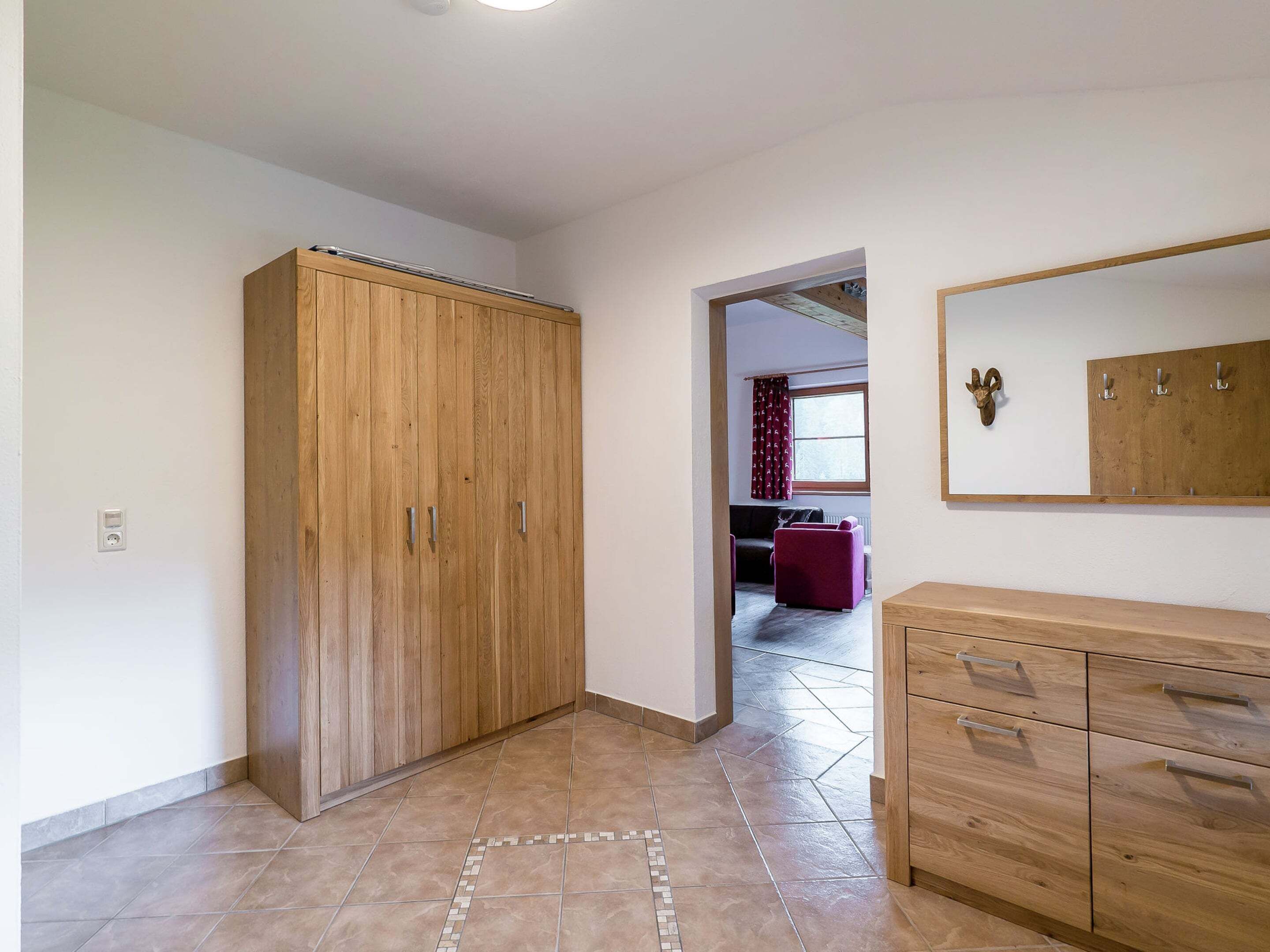 Un couloir avec une armoire en bois, un meuble avec des portes miroir et un sol carrelé.