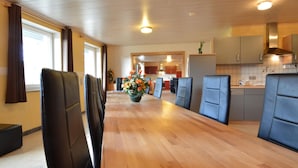 A spacious dining area with a long wooden table and black chairs, a kitchen area with modern appliances, and a view into the dining room. - Apartment in Burg Reuland With Forest (Burg-Reuland)