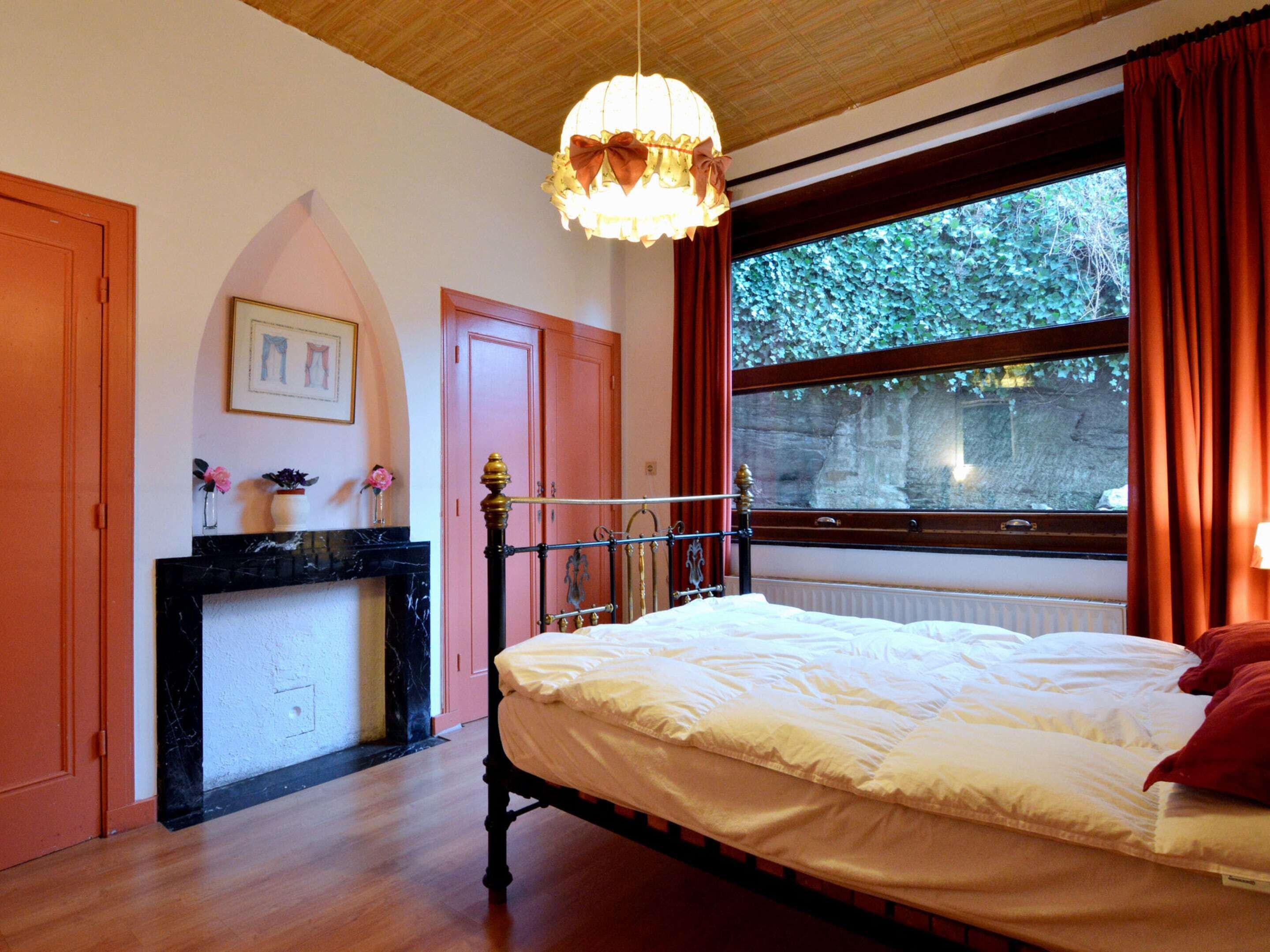 A bedroom with a bed, a fireplace, a window with curtains, and a chandelier.