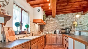 Una cucina con mobili in legno, un muro in pietra, un soffitto in legno e una finestra con tende.