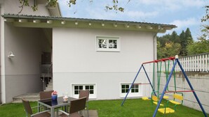A patio with a table and chairs, a swing set, and a building with windows and a staircase. - Cozy Holiday Home in Vandans near Montafon Ski Area (Vandans)