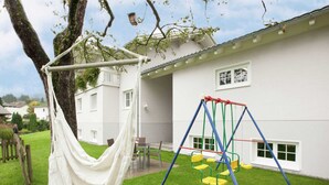 A hammock hanging from a tree, a swing set, and a white building with windows. - Cozy Holiday Home in Vandans near Montafon Ski Area (Vandans)