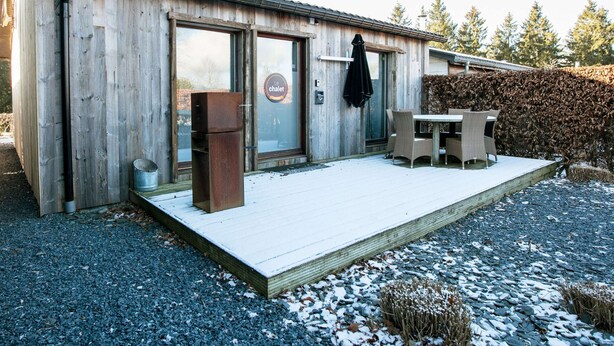 A wooden building with a glass door, a sign reading "Le chalet," and a patio with outdoor furniture. - Boutique Chalet in Büllingen near Lake (Buellingen)