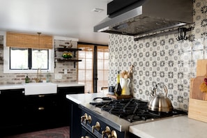 Een moderne keuken met een gasfornuis, zwarte kastjes, een wit aanrechtblad en decoratieve tegels.