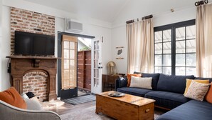 A living room with a brick fireplace, a sofa, a coffee table, and a television. - Palm Cottage San Diego (La Mesa)