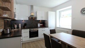 A modern kitchen with white cabinets, a black countertop, a built-in oven, and a dining area with a wooden table and chairs. - Nice Apartment in Detached House with Large Garden near Town Center & Ski Slope (Kotschach-Mauthen)