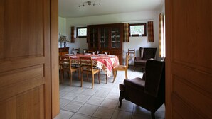 A dining area with a table set for four, wooden chairs, a cabinet with glass doors, and a window with curtains. - Cozy Holiday Home in Lesterny near Lake (Nassogne)
