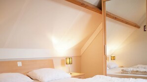 Ein Schlafzimmer mit schrägen Wänden, Holzbalken, einem Bett mit weißer Bettwäsche und zwei Wandleuchten.