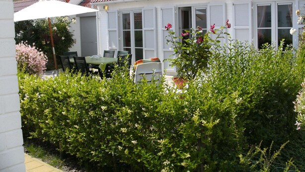 A white building with a red-tiled roof, white shutters, and a garden area with a table and chairs. - Holiday Home in De Haan Near Beach (De Haan)