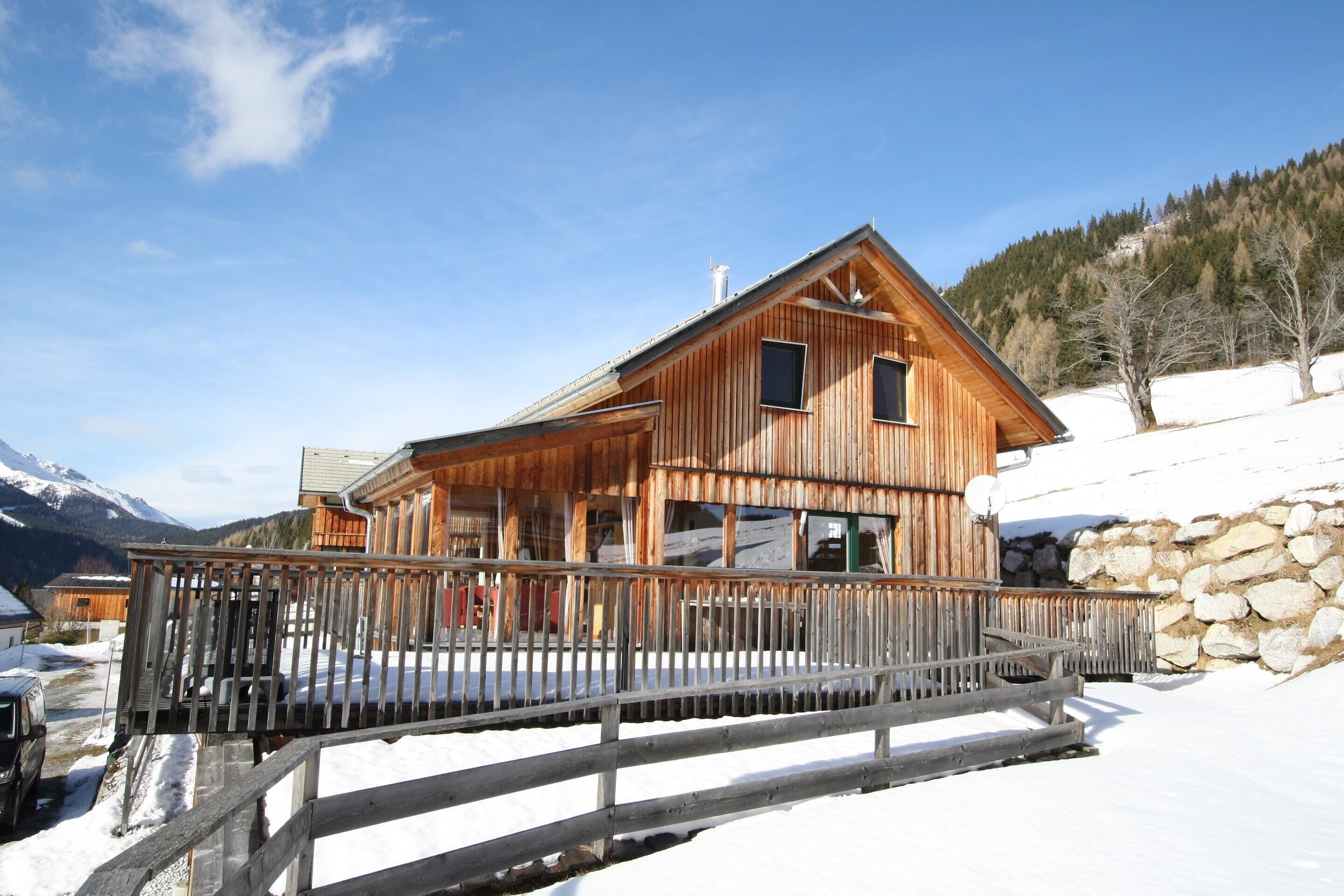 A wooden cabin with a balcony, surrounded by snow and mountains.