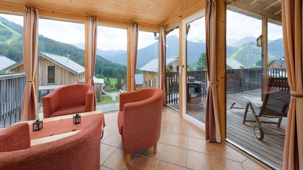 Ein Holzinnenraum mit Balkon, zwei rote Stühle, einem Tisch und Blick auf die Berge.