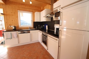 A kitchen with wooden walls, white cabinets, a stove, oven, microwave, and a window with a view of the mountains.