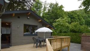 A modern wooden deck with a table and chairs, a white umbrella, and a wooden railing. - Cozy Chalet in Ardennes near Ourthe River & City of Durbuy (Ferrieres)
