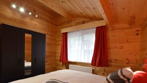 A wooden cabin room with a bed, a window with red curtains, and a radiator. - Cozy Chalet in Ardennes near Ourthe River & City of Durbuy (Ferrieres)