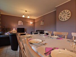 Un comedor con una mesa dispuesta para cuatro, un reloj antiguo en la pared y un televisor al fondo.
