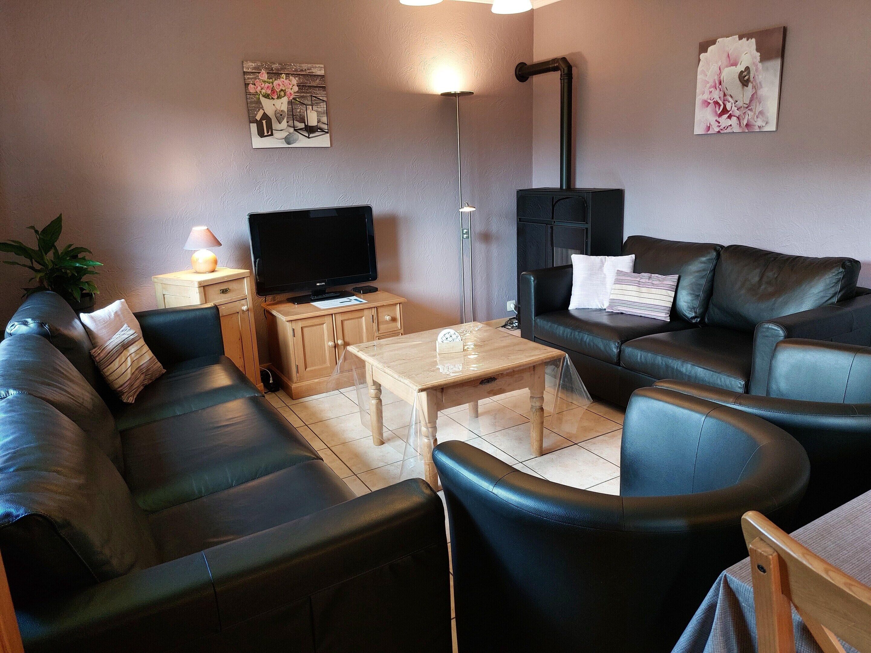 A living room with a black leather sofa, a wooden coffee table, a television, and a black fireplace.