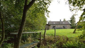 A rustic stone building with a grassy yard and a wooden bridge over a stream. - Elegant Beverce Escape (Malmedy)