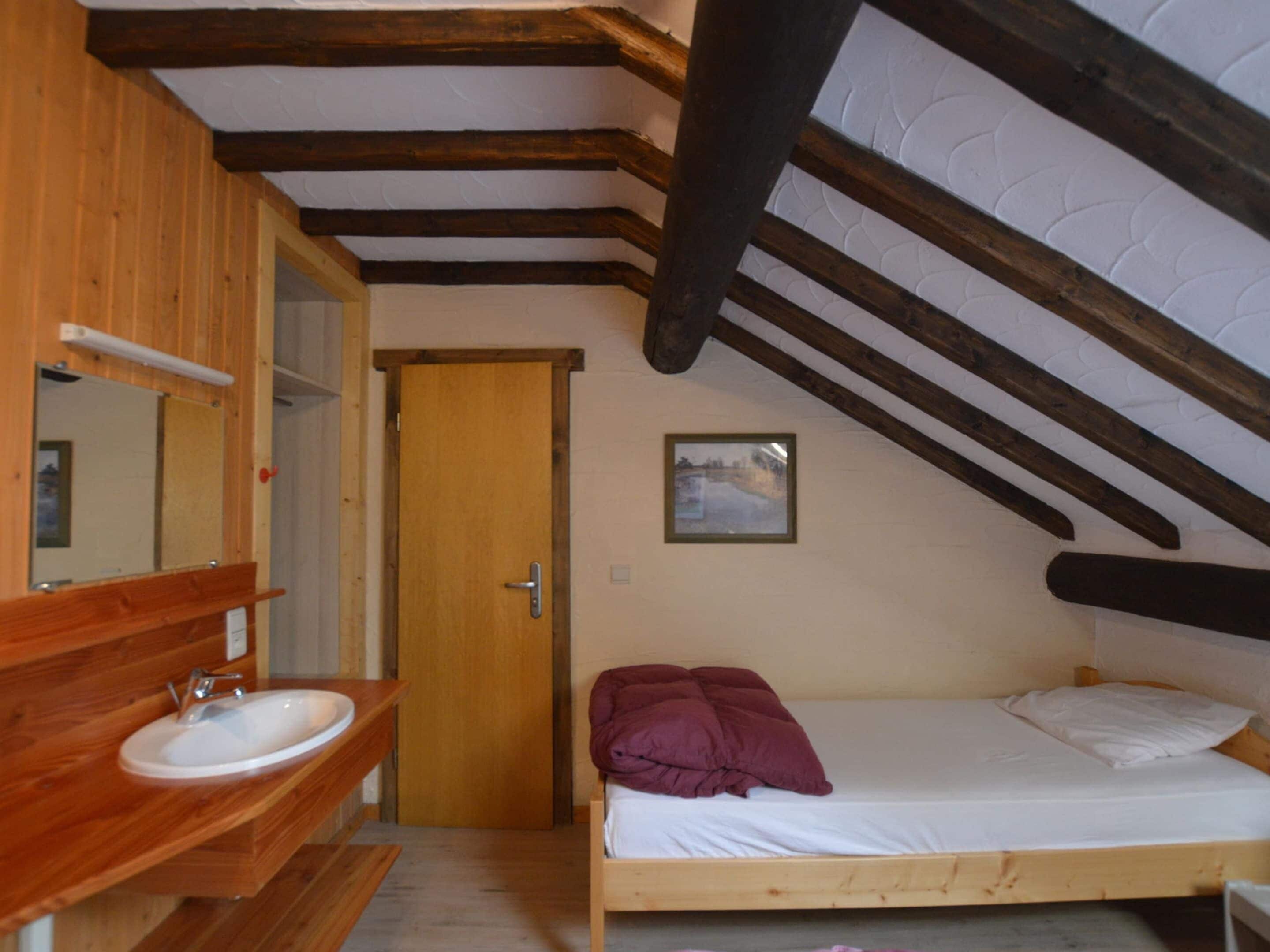 A bedroom with a wooden bed, a white wall, and a wooden ceiling.