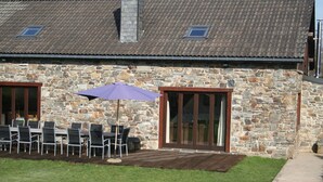 A stone building with a patio area featuring outdoor seating and a purple umbrella. - Elegant Beverce Escape (Malmedy)