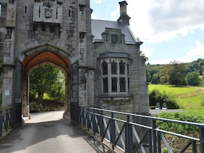 A stone building with a large arched entrance and a window overlooking a green landscape.