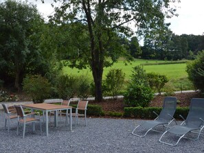 An outdoor seating area with a table and chairs, surrounded by gravel and trees.