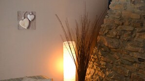 Ein Zimmer mit Steinsturz, einem Bett mit gestreifter Bettwäsche, einer Wanddekoration in Herzform und einer hohen, zylindrischen Lampe.