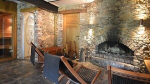 Ein Zimmer mit Stehwänden, einem Kamin, einer Glastür, die nach draußen führt, und einer Sitzecke mit einer Bank und einem Sessel.