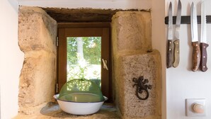 Eine Nische mit Steinwänden, eine Schüssel und einer grünen Netzabdeckung, eine Holztür sowie ein an der Wand befestigtes Messerbrett.