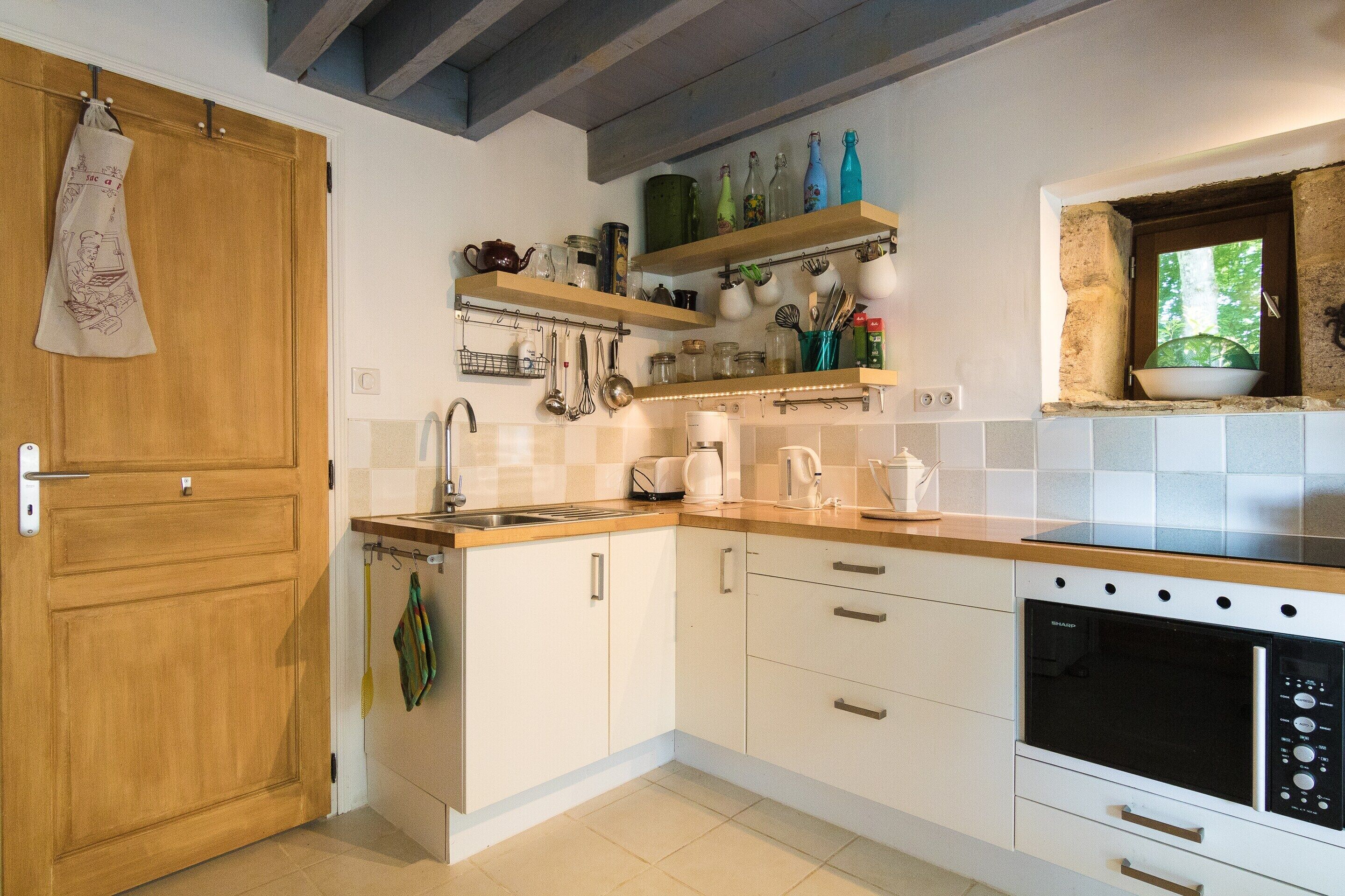 A kitchen with wooden cabinets, a microwave, a sink, and various kitchen utensils on shelves.