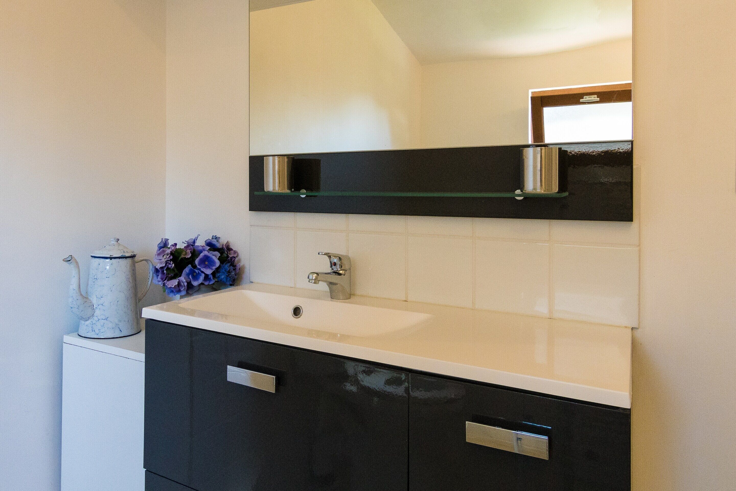 A bathroom with a white sink, dark cabinets, a mirror, and a vase with flowers.