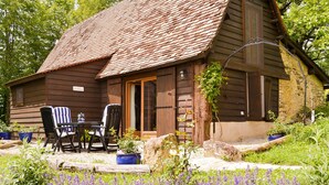 Eine rustikale Holzhütte mit Ziegeldach, einem Esstisch mit Stühlen und einem Garten mit violetten Blumen.