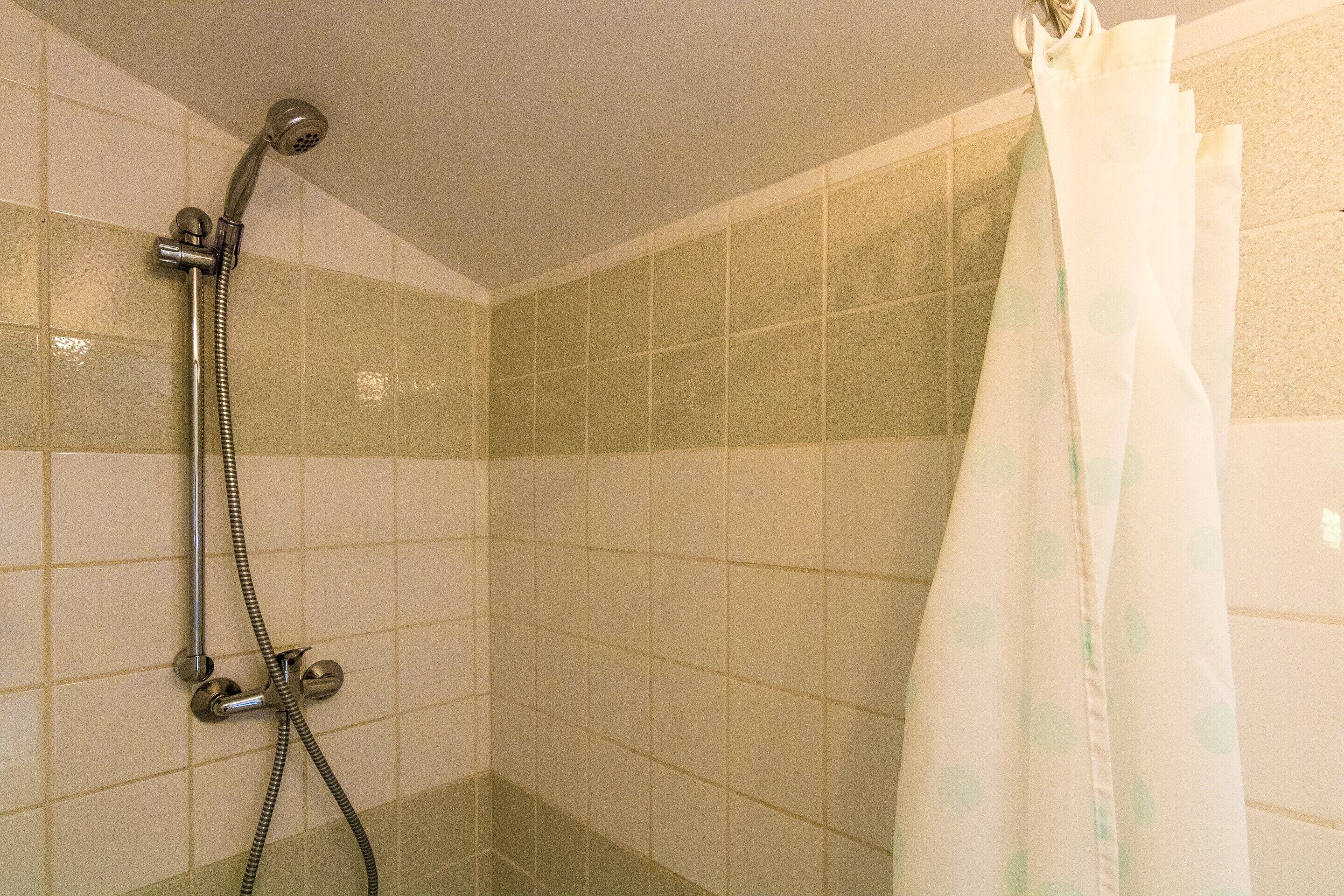 A shower area with a handheld showerhead, a curtain, and tiled walls.