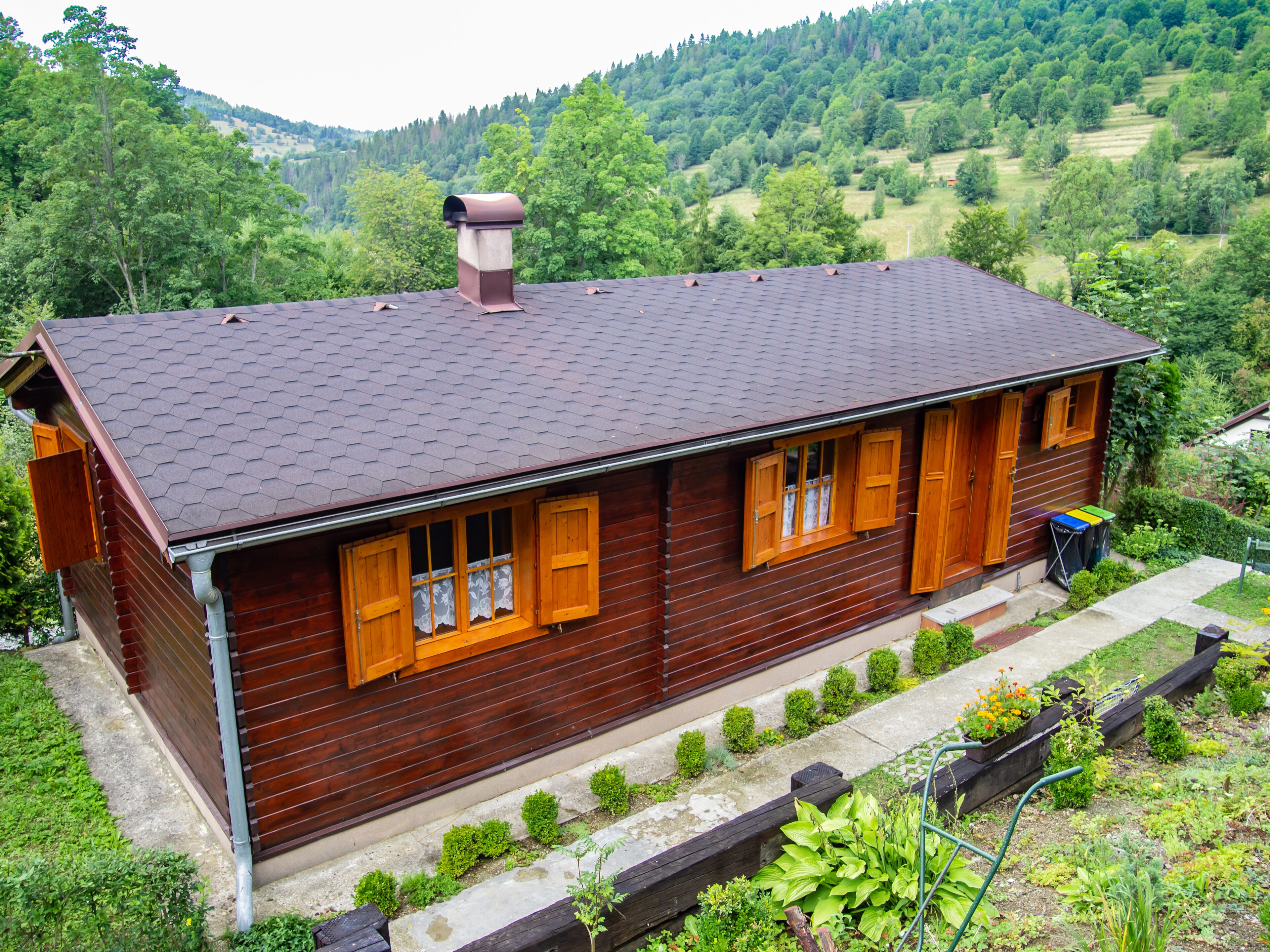 A wooden cabin with a sloped roof, multiple windows with shutters, and a chimney.