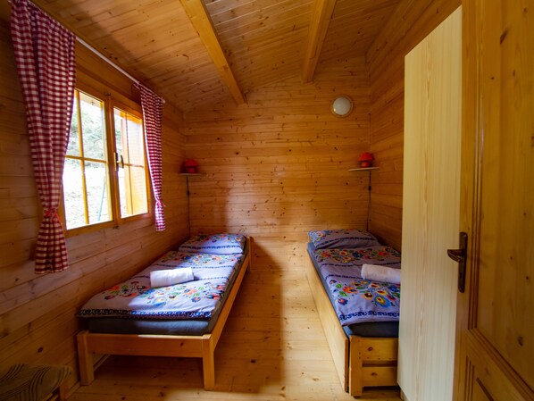 A cabin with two wooden beds, a window with checkered curtains, and a door. - Drevenice Oscadnica (Oscadnica)