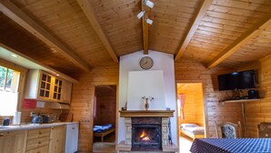 A cozy cabin interior with a wooden interior, a fireplace, a dining area, and a television. - Drevenice Oscadnica (Oscadnica)