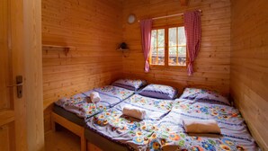 A wooden cabin room with a bed, a window with curtains, and a small shelf. - Drevenice Oscadnica (Oscadnica)
