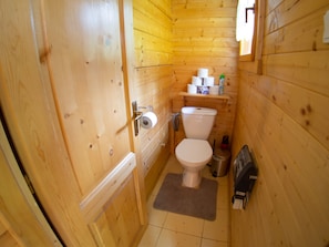 Un baño de madera pequeño y funcional con un inodoro, un estante con papel higiénico y un secamanos.