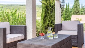 A patio with wicker furniture, a glass table, and a view of the countryside. - Villa in Pouzols With Private Pool & Vineyards (Pouzols-Minervois)