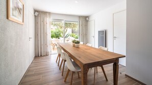 A dining area with a wooden table, white chairs, a potted plant, and a sliding glass door leading to an outdoor space. - Villa in Pouzols With Private Pool & Vineyards (Pouzols-Minervois)