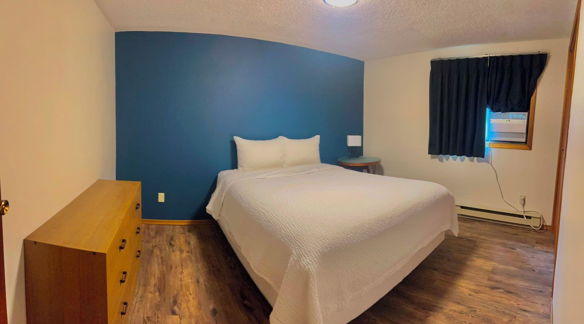A bedroom with a bed, a nightstand, a dresser, and a window with curtains.