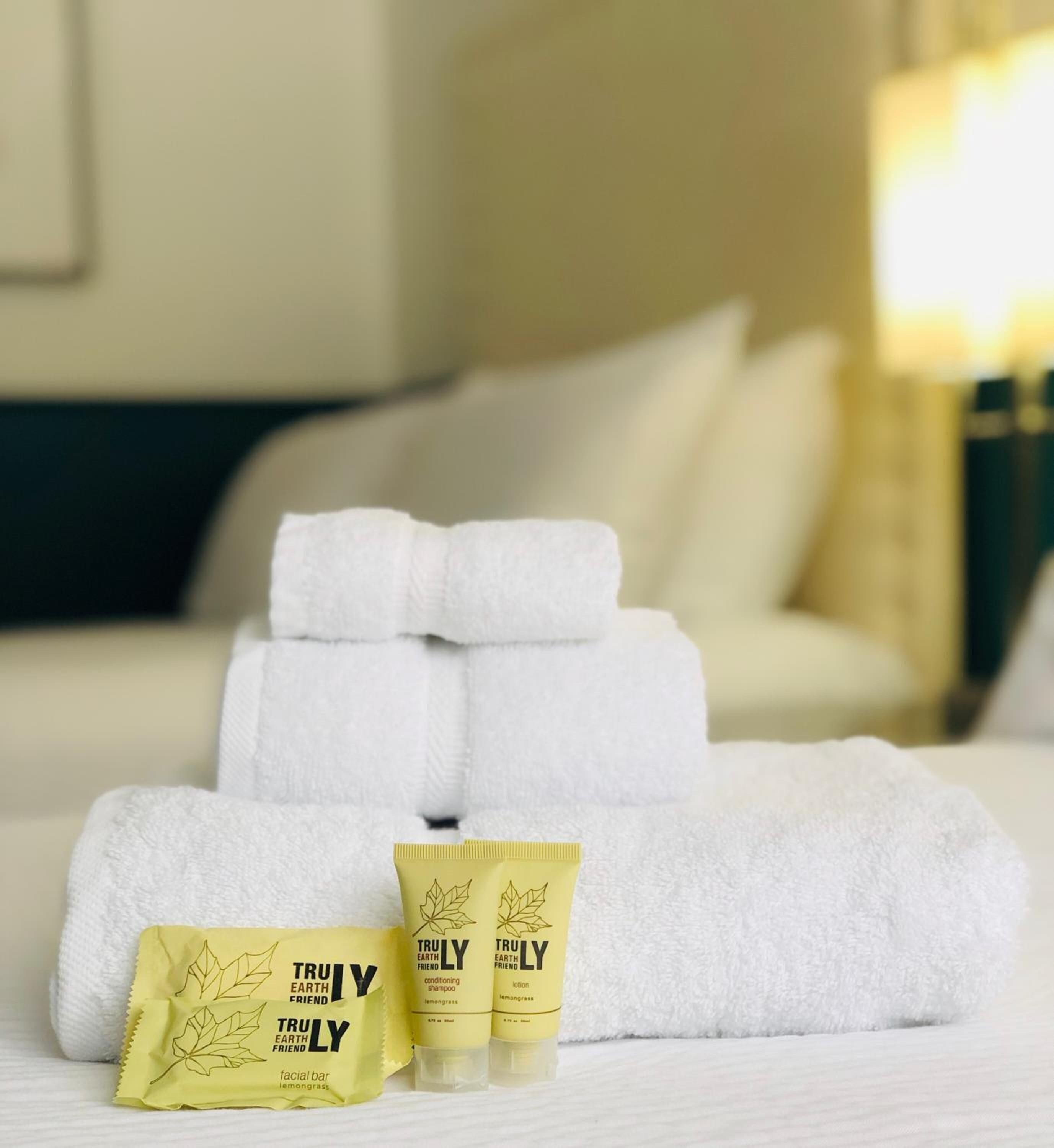 A neatly made bed with white towels and two toiletries labeled 'Truly Earth Friend.'