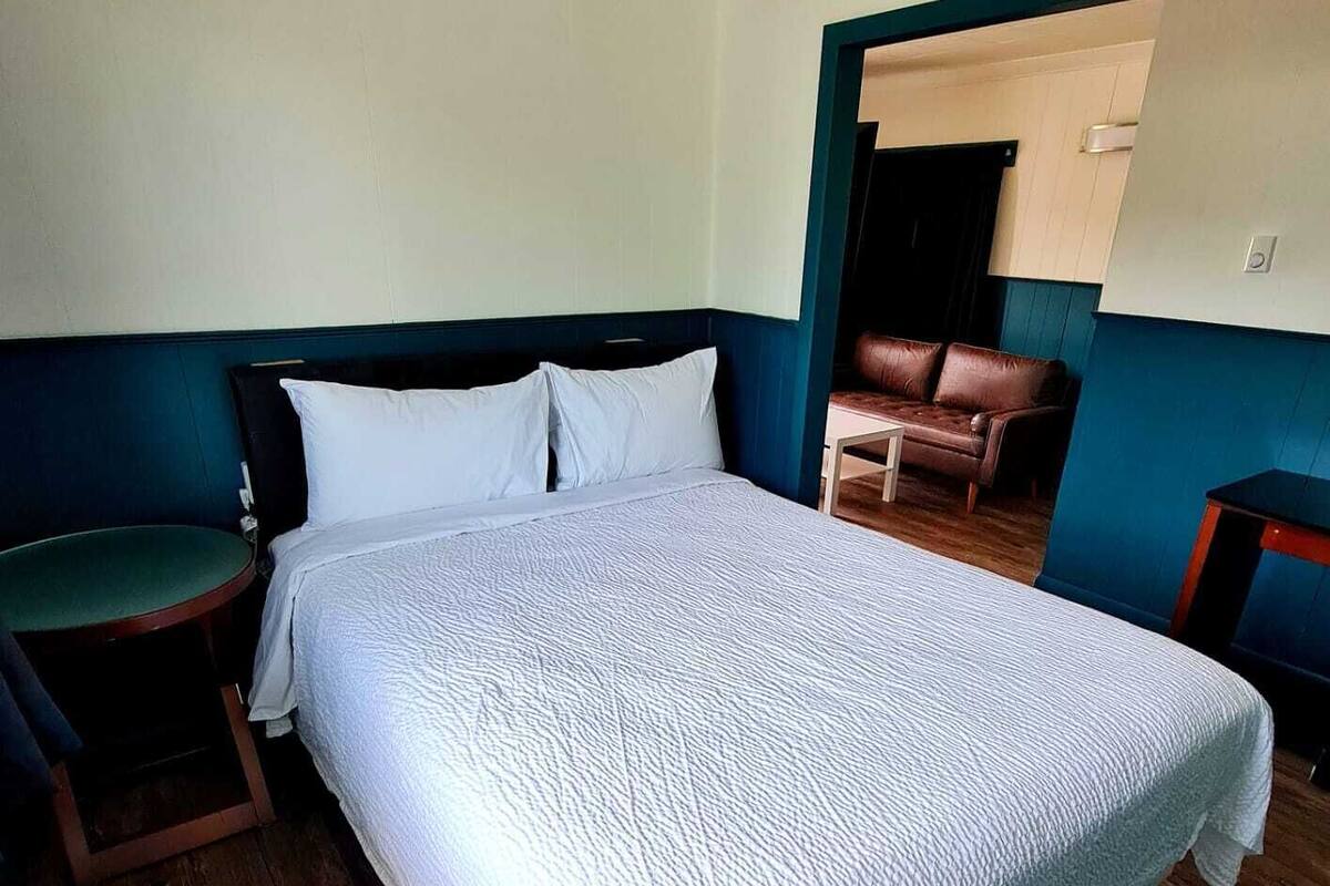 Quarto com uma cama grande, uma cadeira verde, piso de madeira e um sofá de couro marrom ao fundo.